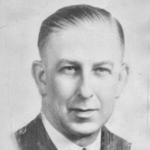 White man in suit jacket and tie with slicked back hair