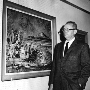 white man in suit looking at painting on wall