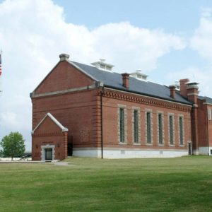Multistory brick building with covered porch framed windows and flag pole on grass