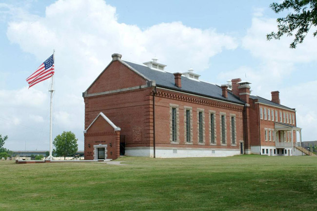 Multistory brick building with covered porch framed windows and flag pole on grass