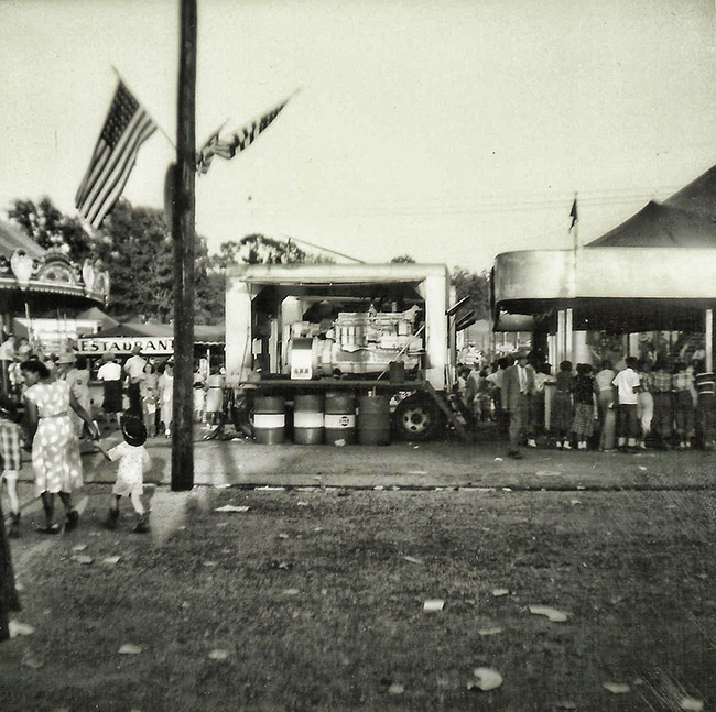 Crowd at fair with carousel restaurant and building with canopy