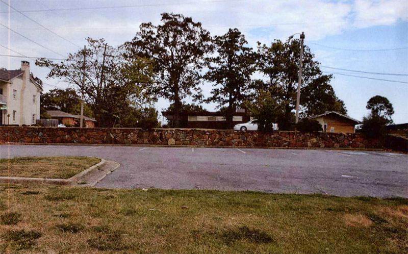 Stone wall with parking lot in the foreground and houses beyond the wall