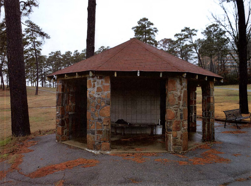 Hexagonal shelter with rock columns and bench inside surrounded by golf course