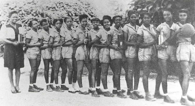 African-American girls in matching basketball uniforms with shorts standing in line with African-American woman in skirt