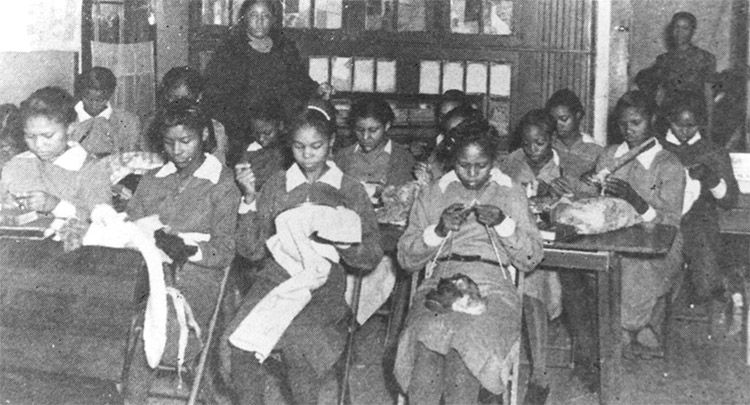 African-American girls sitting in sewing class with African-American woman standing behind them