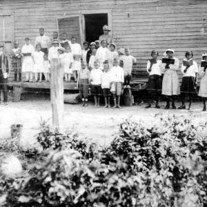 African-American men and women posing with students outside school house with barbed wire fence and garden