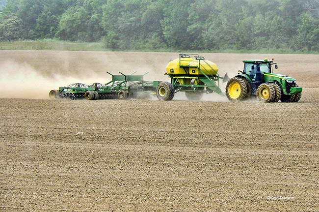 Green tractor pulling planter and tiller trailers in field