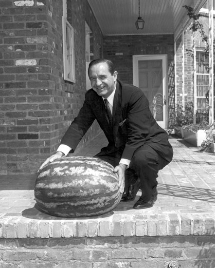 White man in suit and tie posing on a porch with a large watermelon