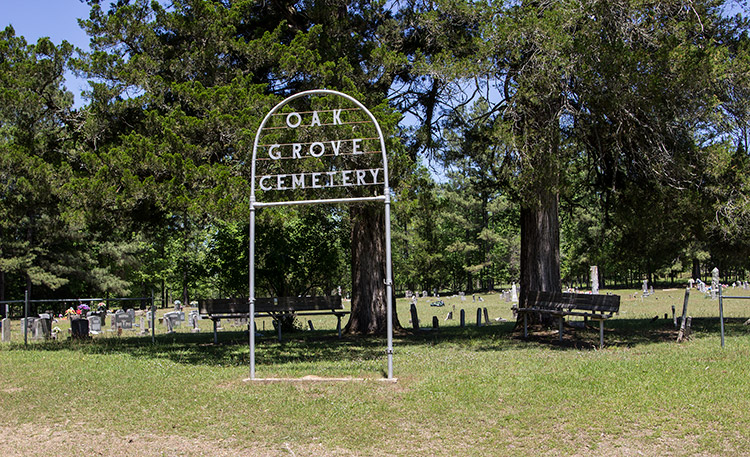 Iron arch sign and benches with tree outside cemetery