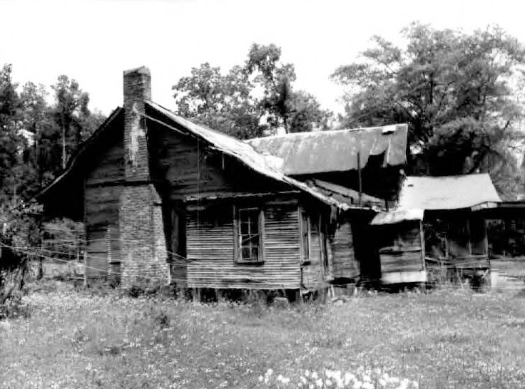 Side view of dilapidated single-story house with screened-in back porch and brick chimney