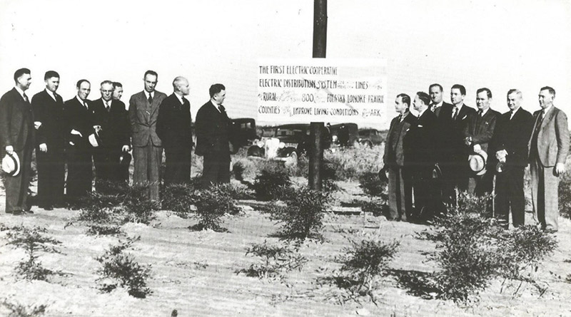 Groups of white men in suits on either side of sign on pole