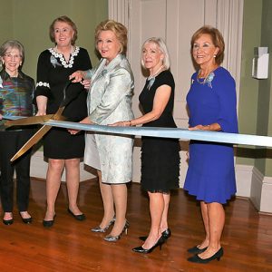 Group of older white women indoors cutting a ribbon with large scissors