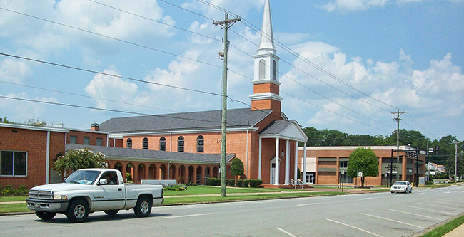 White truck driving down street past brick building with steeple and covered walkway