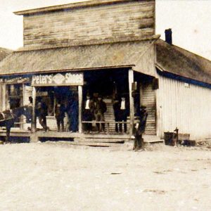 White men standing on covered porch of store with horse and buggy tied to post