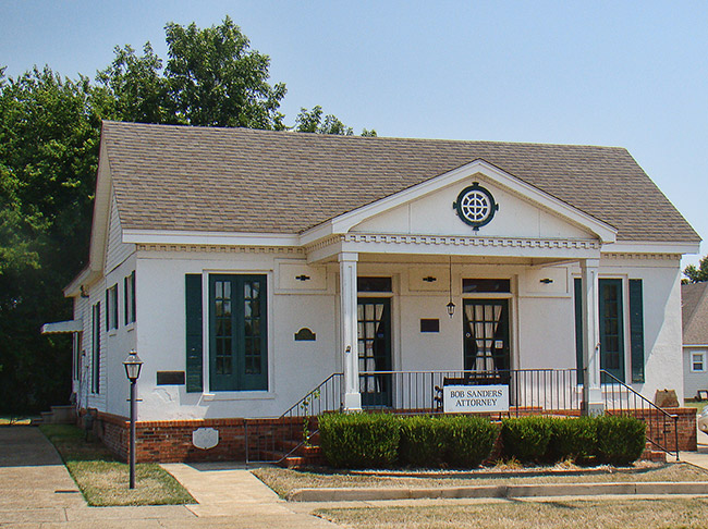 Single-story white building with two columns on porch and two sets of doors and windows