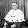 White man in bishop's robes sitting with curtains behind him