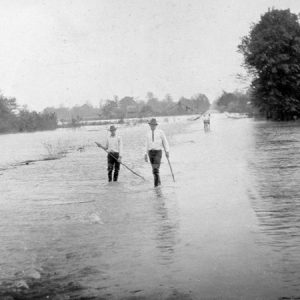 Two white men wearing hats walking on flooded streets