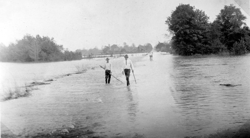 Two white men wearing hats walking on flooded streets