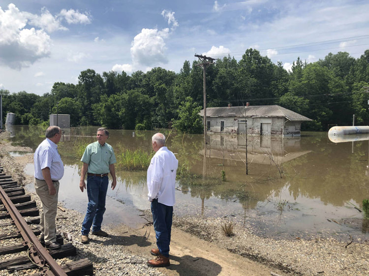 Three white men standing by railroad tracks observing flooded depot facility