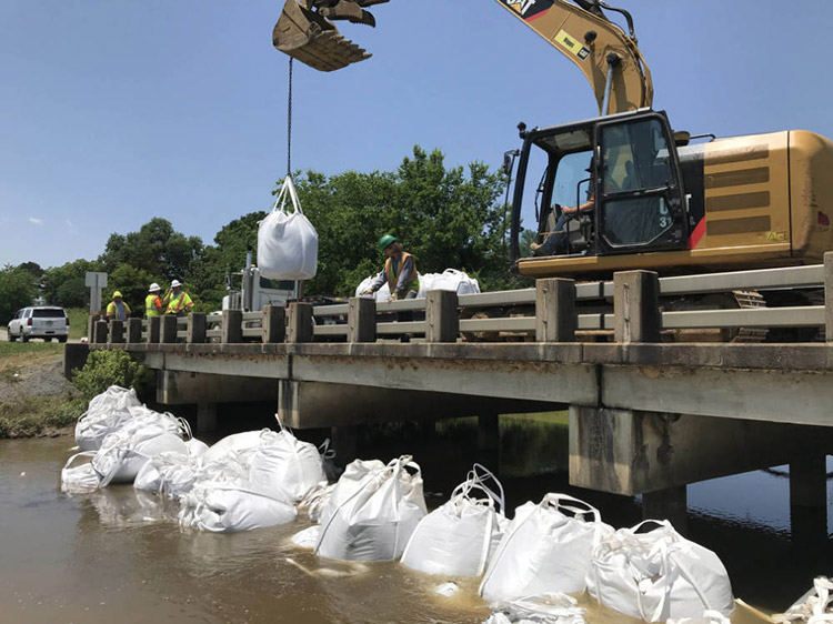 Sandbags being lowered off of a concrete bridge by an excavator to prevent flooding