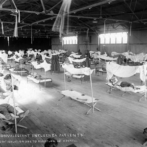 White patients sleeping on cots in airplane hanger