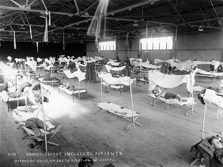 White patients sleeping on cots in airplane hanger