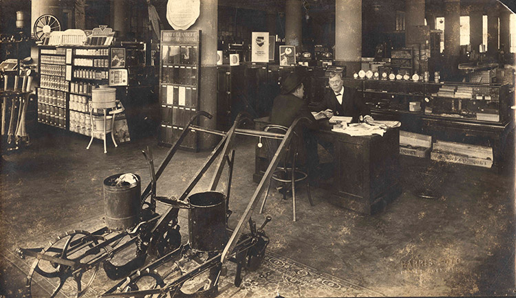 Pair of plows on floor of hardware store with men at desk and shelving in the background