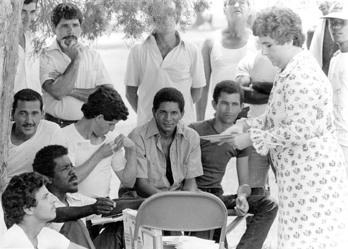 White woman talking to a group of Cuban men standing and sitting under a tree