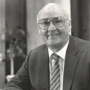 Older white man with glasses smiling in suit and tie
