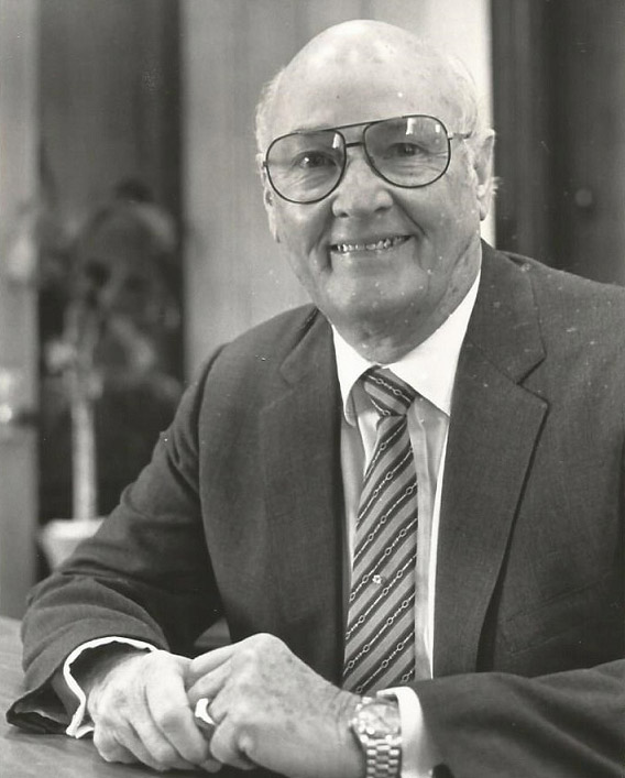 Older white man with glasses smiling in suit and tie