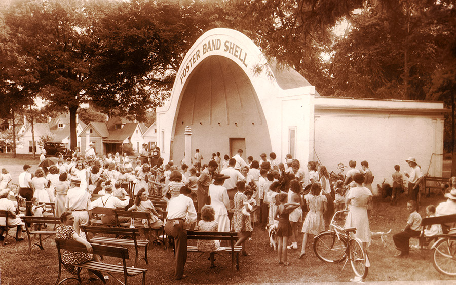 White crowd seated and standing around "Foster Band Shell" stage building in city park