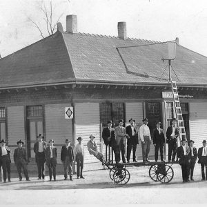 Group of white men and wheeled cart outside railroad depot building