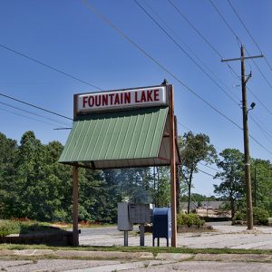 "Fountain Lake" sign with green awning over mailboxes in parking lot with power lines crossing above it