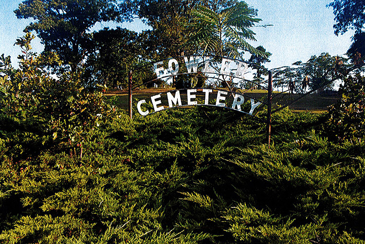 "Fowler Cemetery" sign on iron arch frame in bushes