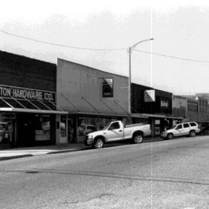 "Benton Hardware Company" and other brick storefronts on street with parked vehicles