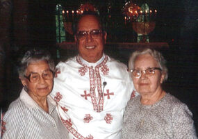 White man in white clerical robes with two older white women in dresses