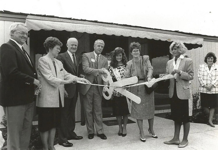 Group of older white men and women cutting a ribbon with giant scissors