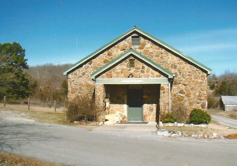 Stone church building with covered entrance and green front door