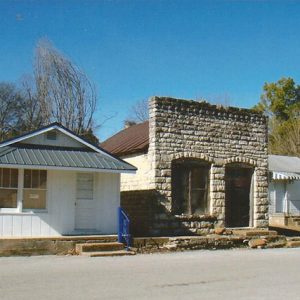 Single-story stone storefront between two single-story buildings with white siding