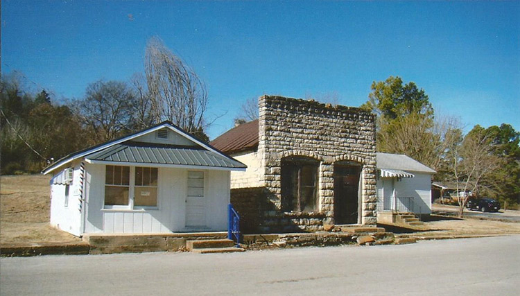 Single-story stone storefront between two single-story buildings with white siding
