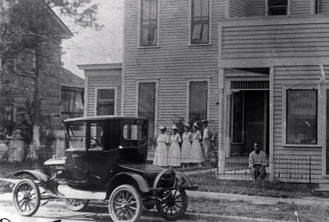 African-American men and nurses outside multistory wooden building with car parked on the street