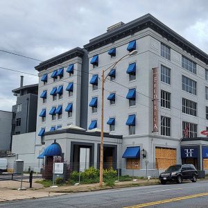 Multistory hotel building with blue awnings and boarded up first floor windows on two-lane road