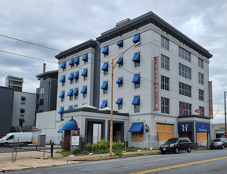 Multistory hotel building with blue awnings and boarded up first floor windows on two-lane road