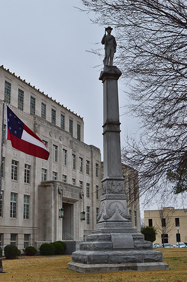 Stone monument with soldier holding gun atop a pedestal next to flag