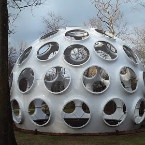 White geodesic dome with round holes and bare trees in the background