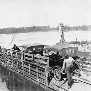 Men loading two cars onto river ferry