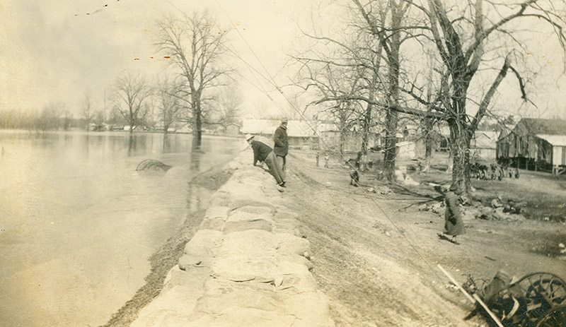 Two men examining levee next to overflowing river