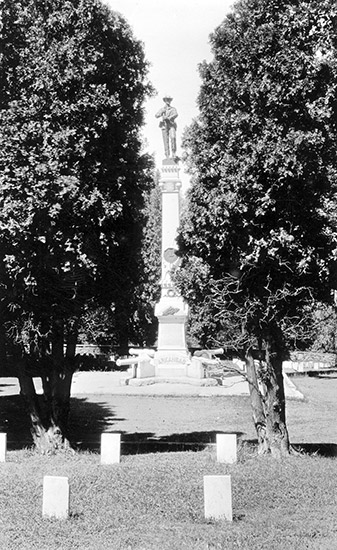 Soldier on tall obelisk shaped monument between two trees