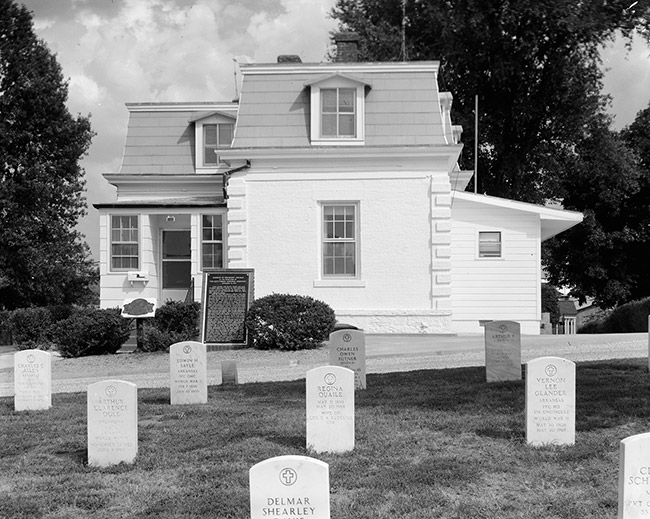 Two-story building with plaque and gravestones in front
