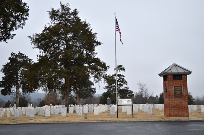 Trees flag pole and brick tower with plaque in cemetery